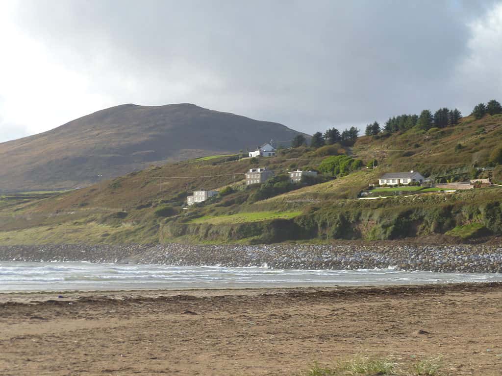 a sandy beach meets the sea with green hills and mountains in the background at Inch Beach in Ireland.  One of my Ireland travel tips is to visit lesser-known places