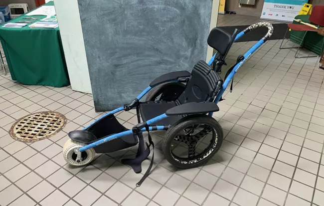 A black and blue manual wheelchair designed for kids.  There is a high back with head rest, two large wheels in the back with one small wheel in the front.