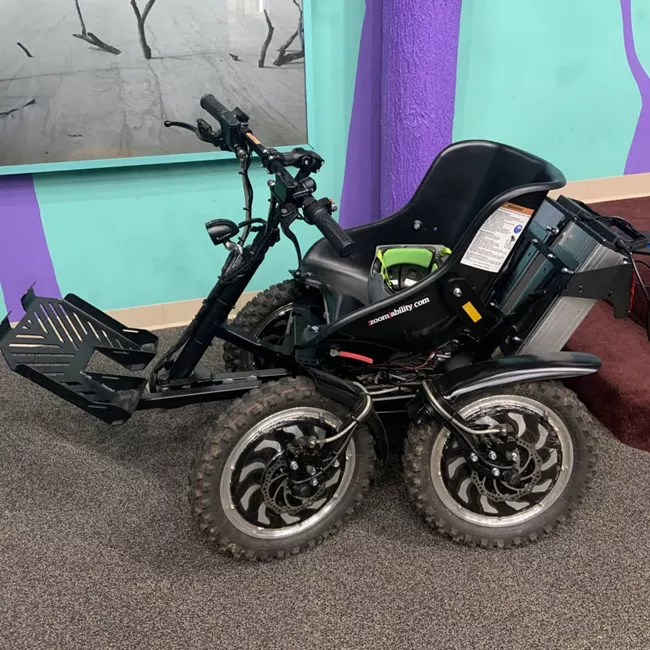 a large four wheeled device that is motorized and steered by a handle bar in the front.  This is a wheelchair that is adapted for hiking