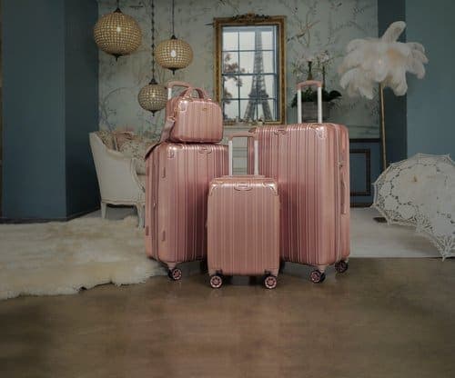 a set of 4 pink suitcases are on a wooden floor in front of a window in a white walled room