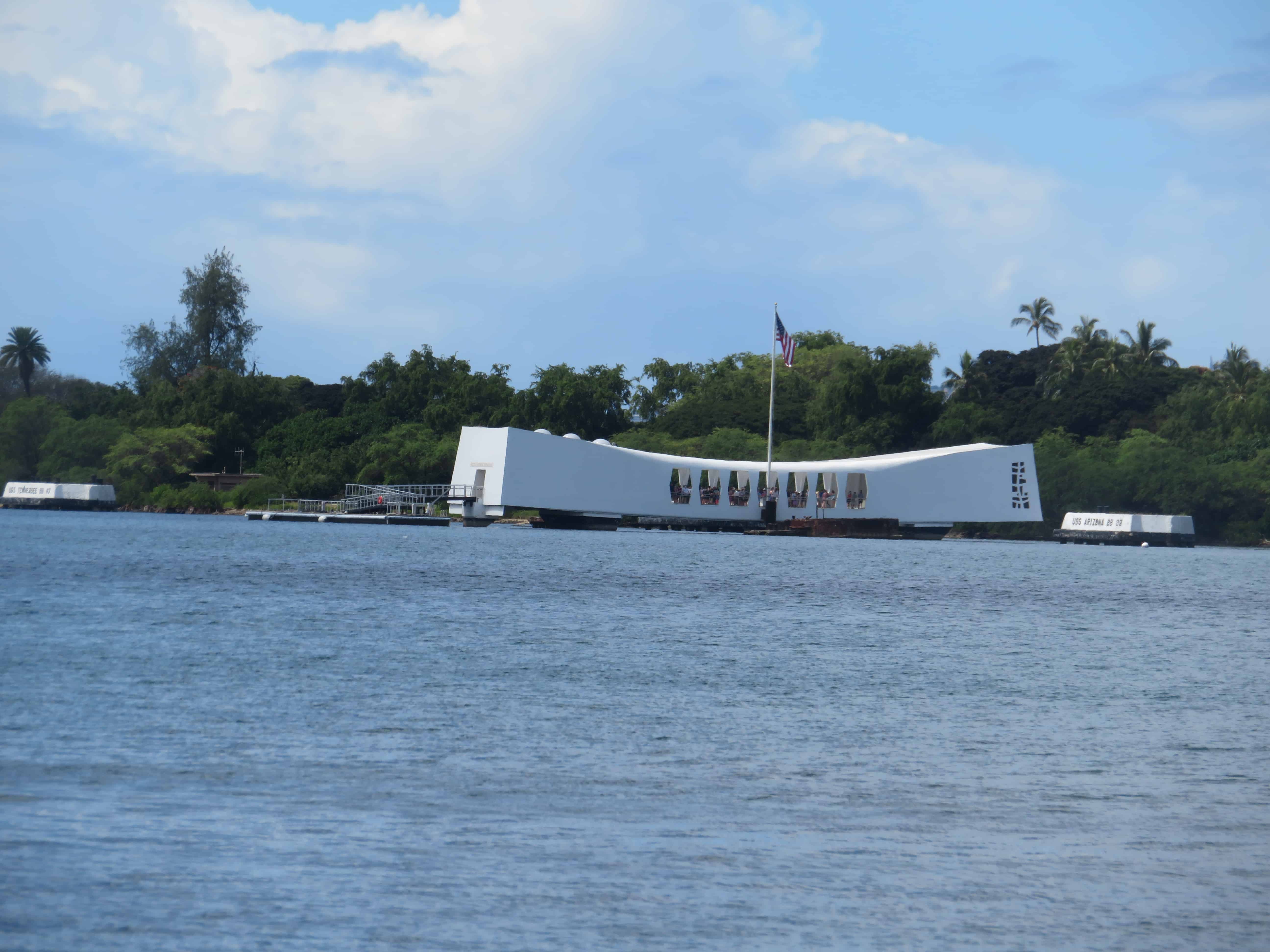 A white rectangular structure sits on top of a blue watered bay. The USS Arizona Memorial in Oahu