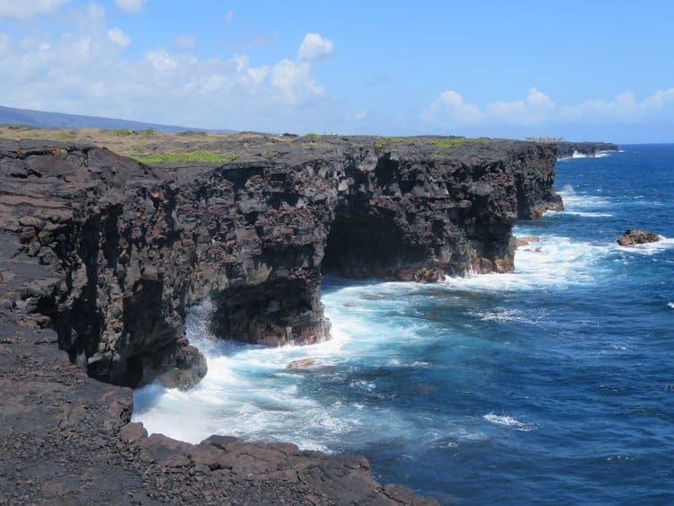 Grassy land becomes a black cliff that drops off into the ocean. Sea arches are along side of the cliff