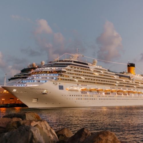 a cruise ship sits in the water by a rocky coast. It is dusk