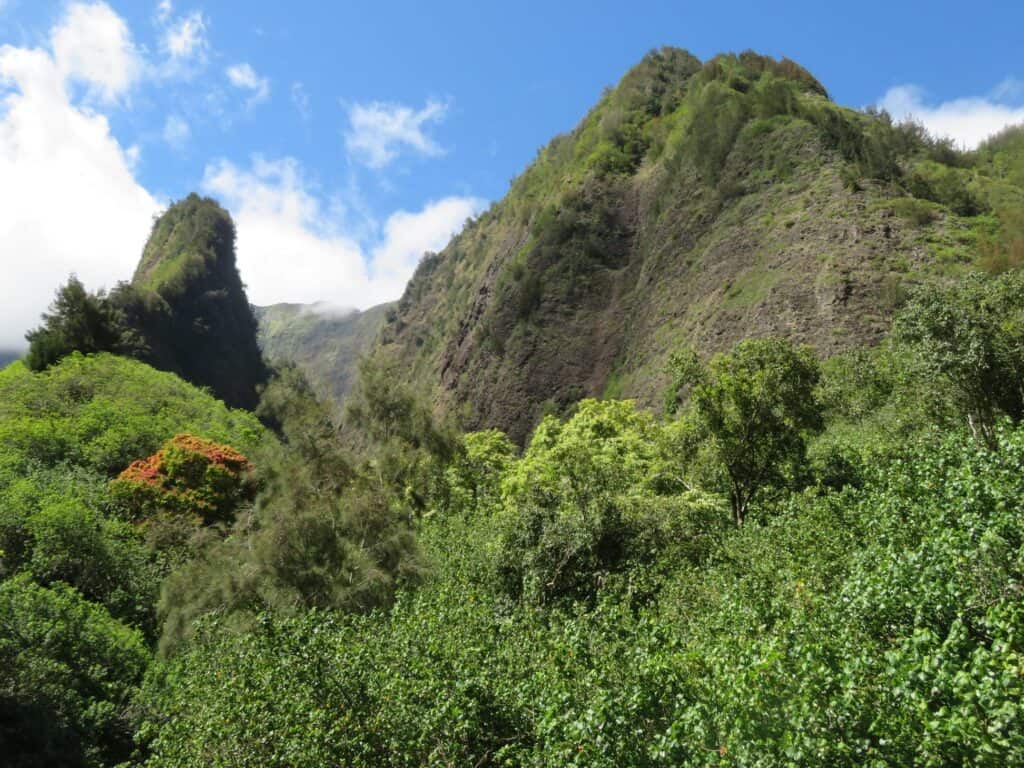 A lush green grassy area is beneath a pointed green mountain.  To the left is another more narrow and smaller pointed mountain