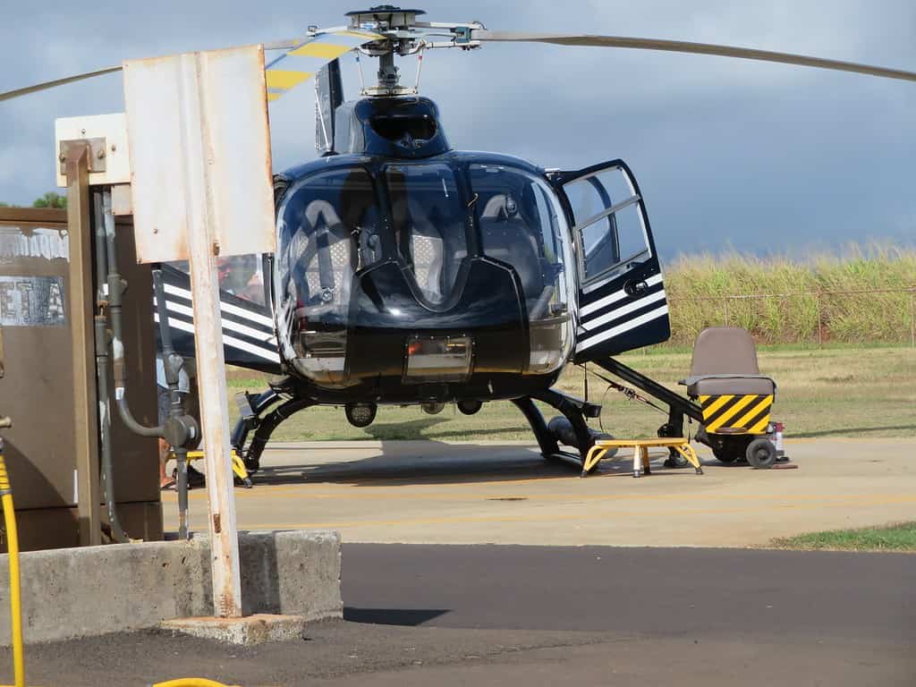 a black helicopter is sitting on a helipad with the doors open.  A ramp with a grey chair is on the right side of the helicopter and connected to the back door.