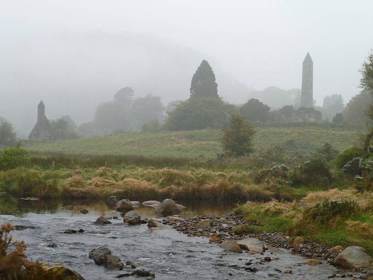 A misty morning in accessible Ireland. A stream is in the foreground and in the mist are the remains of an old church.  My Ireland travel tips include getting out of Dublin.