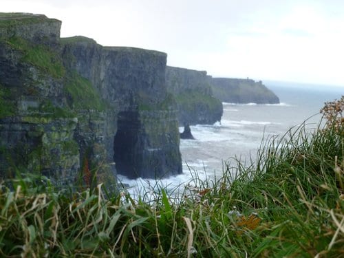 The cliffs of Moher tower over the ocean. One of the cliffs has a sea arch in it.