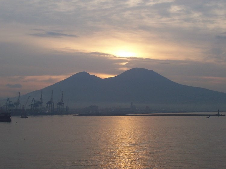 The ocean is in the foreground wiht My Vesuvius behind it on a cloudy day at sunrise.