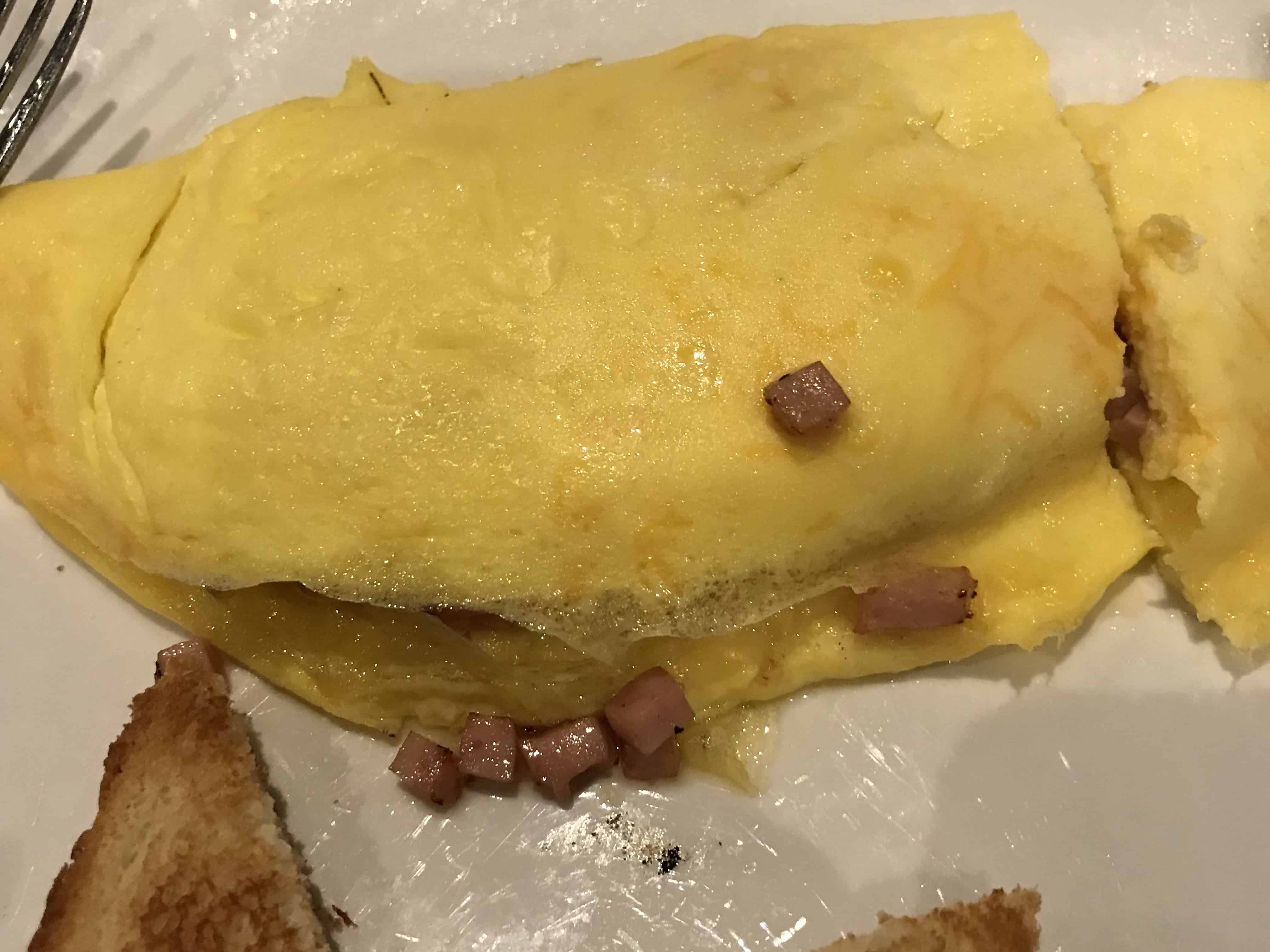 a white plate has a ham and cheese omelet on the top with two pieces of white toast at the bottom