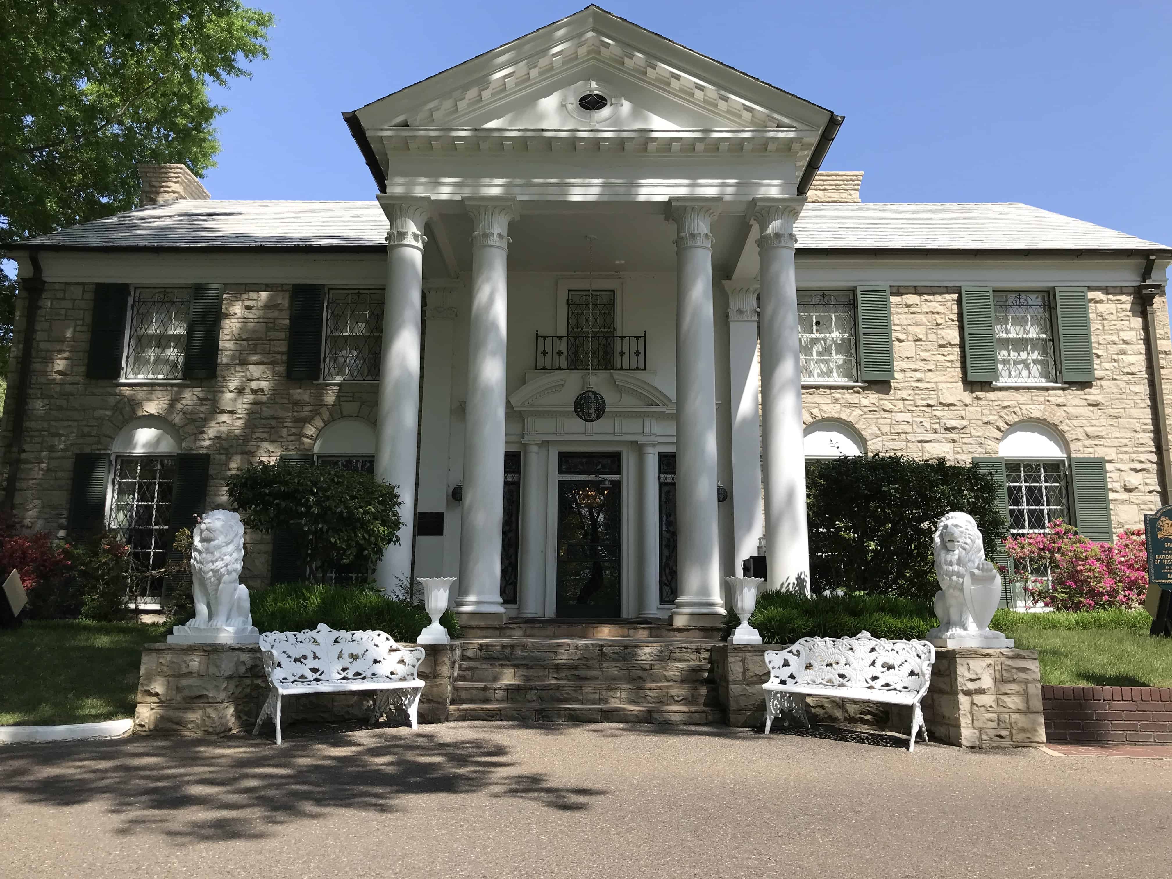 A large two story home with green shutters and tall white columns at the staired entrance make up Graceland which was once home to Elvis