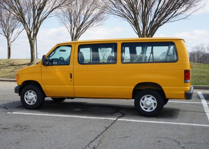 a large, bright yellow van is parked in a parking lot with three trees in the background