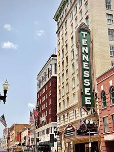 a sunny day with pink and red buildings lining a street on the right.  A black sign with white letters says Tennessee