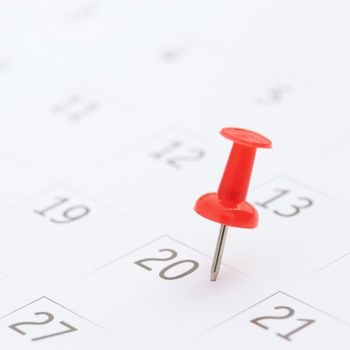 a white calendar with a red push pin on one of the days