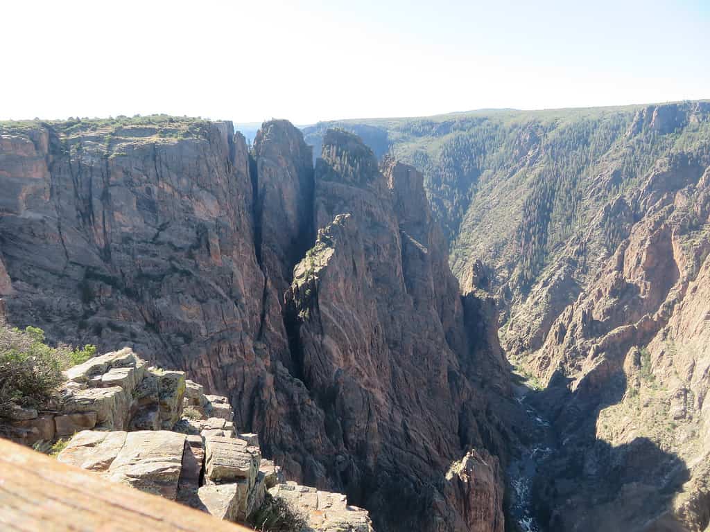 View of the Black Canyon of the Gunnison from a north rim overlook. Rock formations protrude from the left side of the canyon with the Colorado river at the base of the canyon