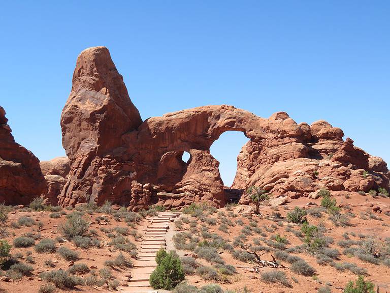 In Arches National Park, a vertical rock formation is on the left attached to an arch