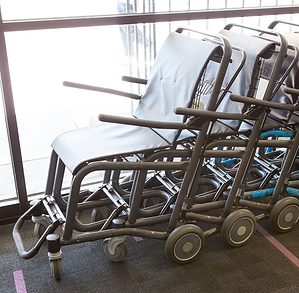 Three aisle wheelchairs form a line in front of a window at an airport