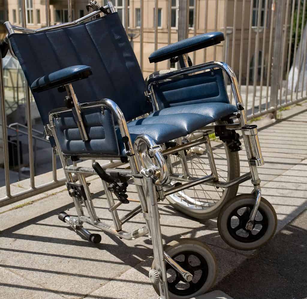 a manual wheelchair with a blue cushion seat is missing the large left wheel at the back 