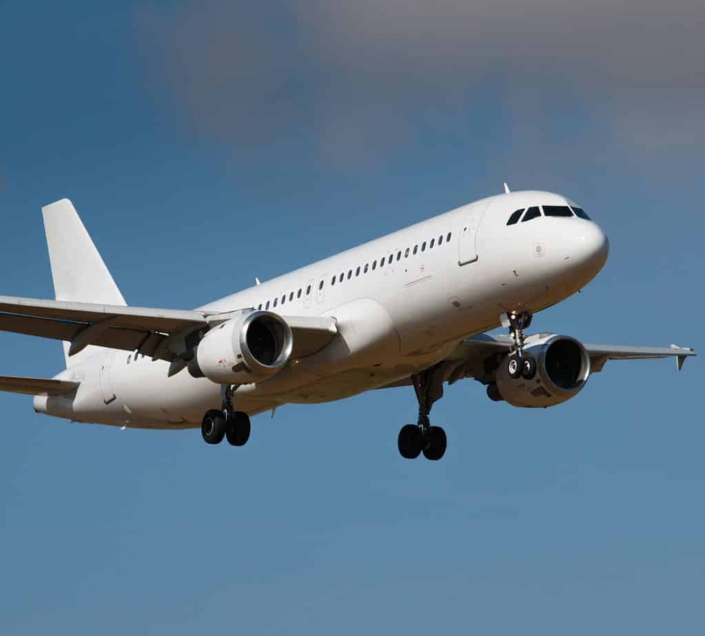 a white airplane flies against a blue sky.