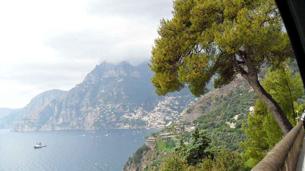 A tree is on the right side in the foreground. Beyond the tree is the sea and the Amalfi Coast on the way to Positano