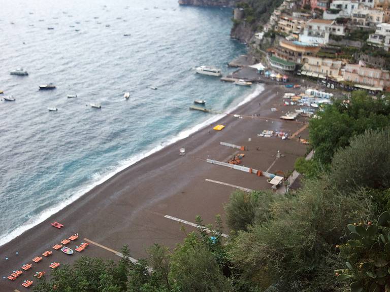 a dark brown sandy beach meets the water along the Amalfi Coast in Positano Italy.  