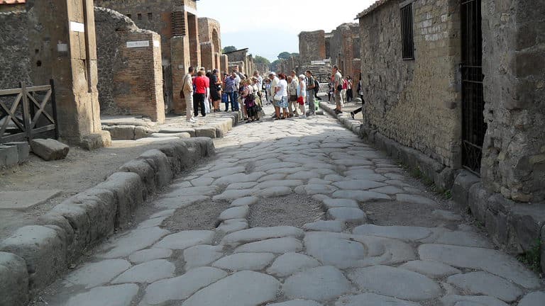 A large cobblestoned street runs between two buildings that are in ruins at Pompeii.  Pompeii is one of the sites in this Rome and Amalfi Coast itinerary