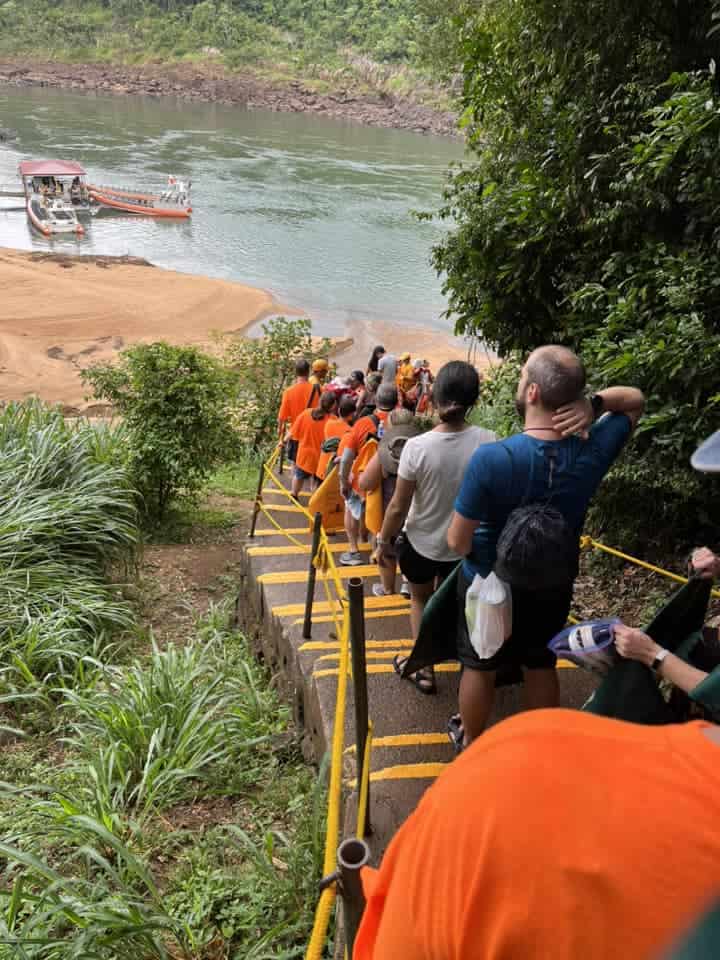 A large group of people descend a steep stairway of brown steps with yellow edges.  Ropes on either side of the stairs act as railings