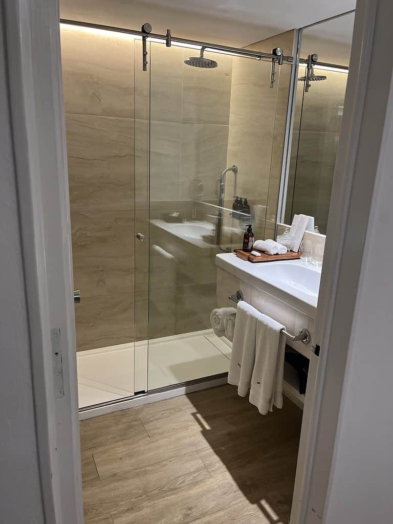 The bathroom in a jungle view room at the Gran Melia Iguazu hotel.  There is a shower with a small step to enter and a white sink in front of the shower