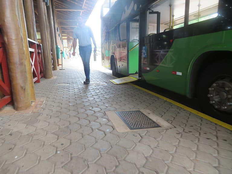 A green double decker bus is pulled along side a sidewalk and has a ramp coming out of the doorway