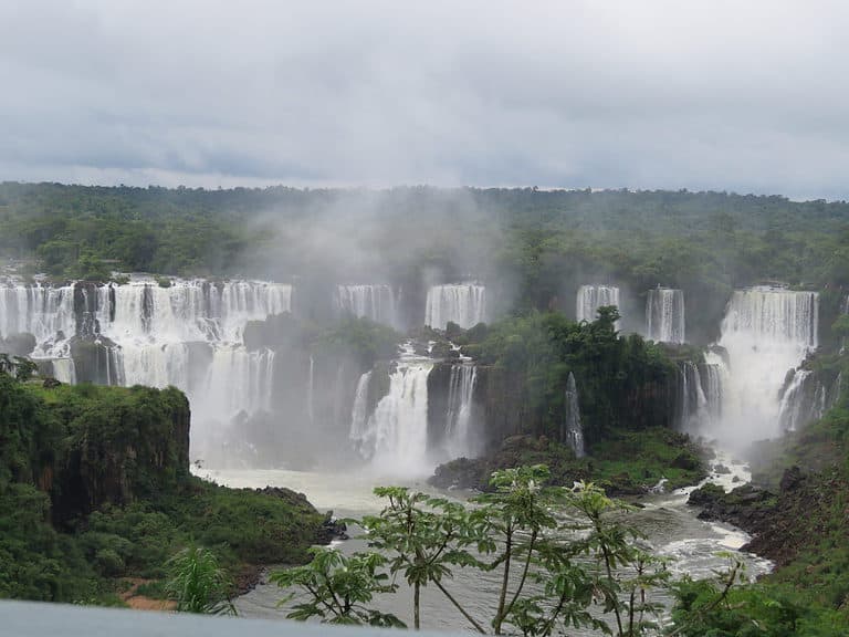 On the Brazilian side of Iguazu Falls, an overlook depicting a large wall of rocks which contains many different waterfalls flowing into a river