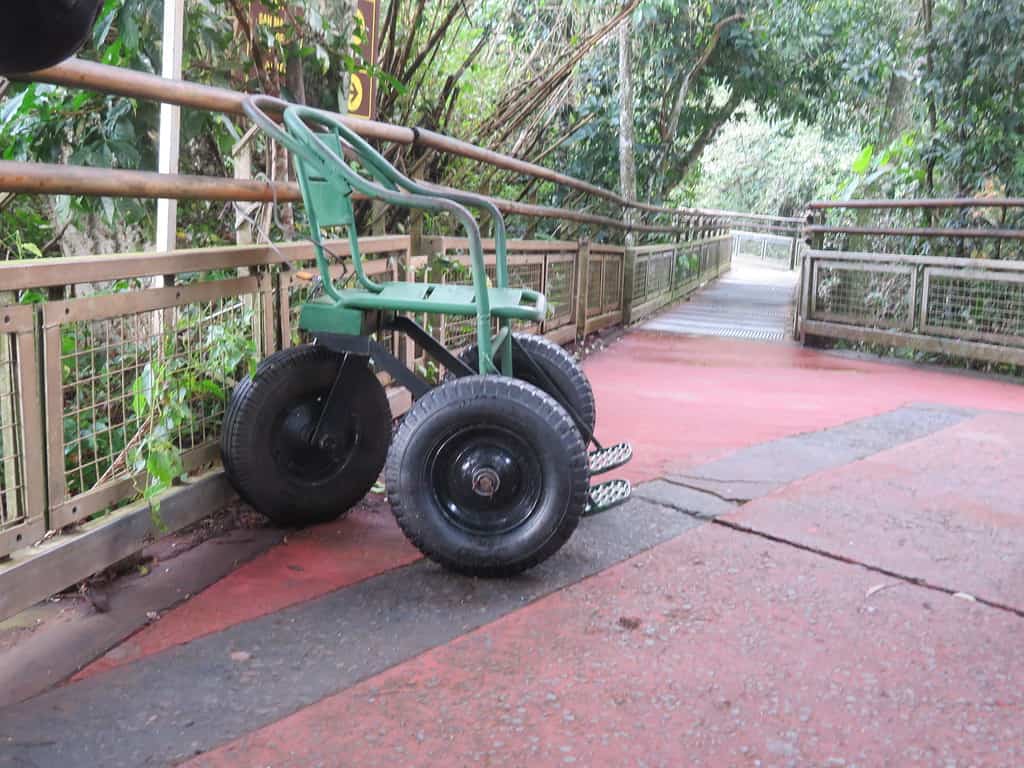 A green metal chair with three large black tires sits on red pavement