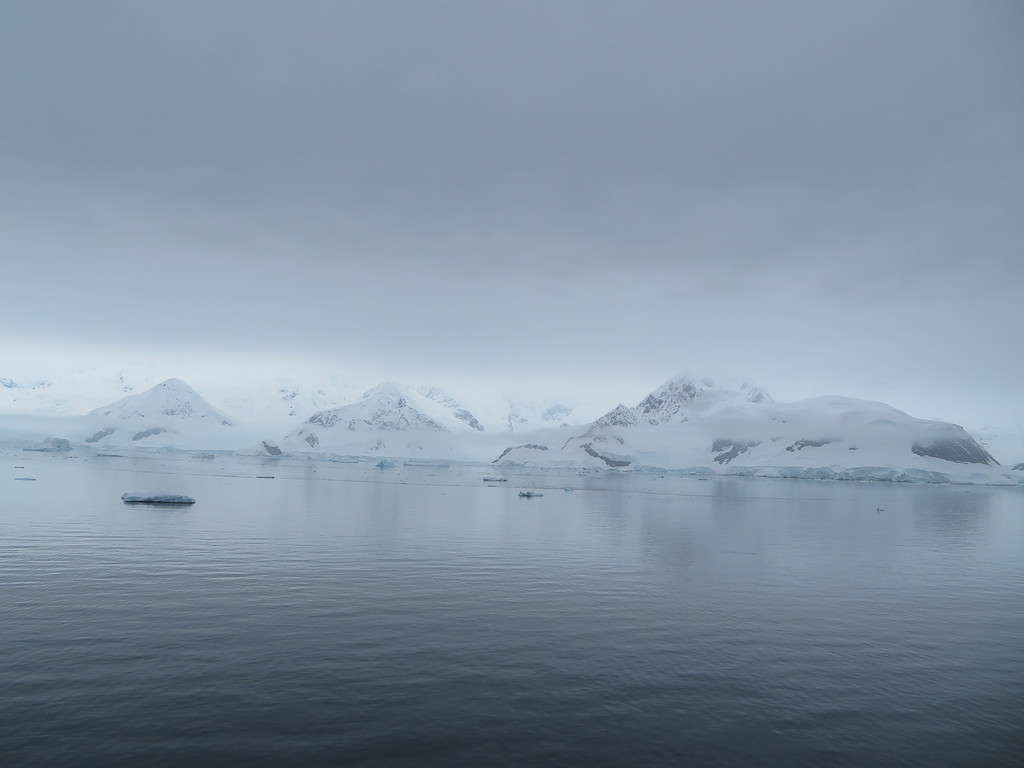 A snow-covered mountain range emerge from the ocean in Antarctica under a grey sky