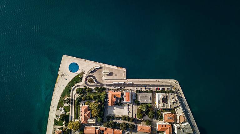 Blue Green water in Zadar Croatia has a portion of the city jutting out into it.  THere is a paved pathway that outlines the city.