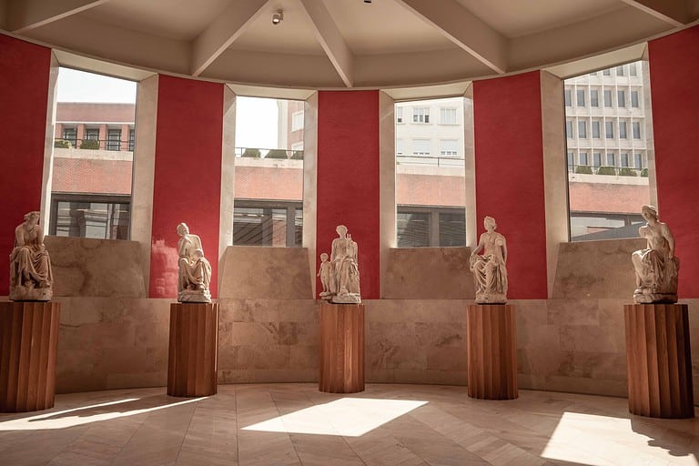 5 sculptures sit on wooden pedestals against a red wall with windows at the Prado Museum