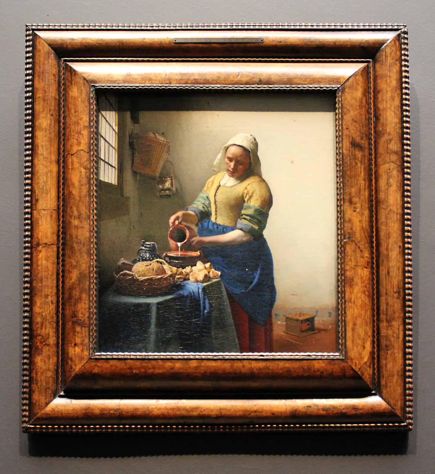 A framed picture of "the milkmaid" painting by Johannes Vermeer sits against a grey wall in one of the best art museums in Europe.