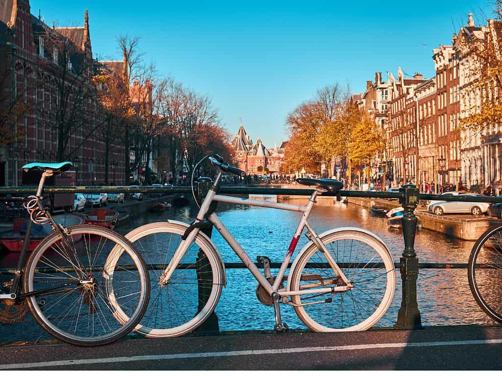 three bikes sit propped against a metal railing on a bridge and overlook a canal in Amsterdam.  Taking a bike tour is a popular Amsterdam tourist attraction.