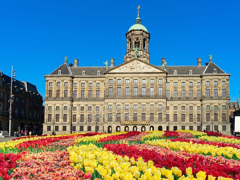 The exterior of the Royal Palace in Amsterdam with a field of colorful tulips in front of it.