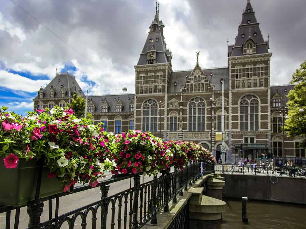 a brown brick building with white trim and two central towers make up the Rijksmuseum Art Museum which is one of the tourist attractions in Amsterdam