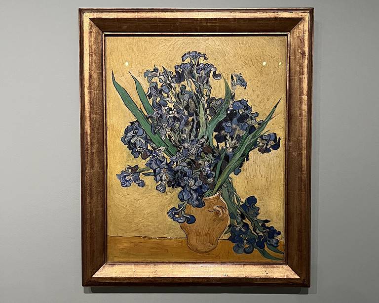 a painting of purple flowers with green leaves in a yellow vase sits on a golden background and is located in the Van Gough Museum in Amsterdam which is considered to be one of the best art museums in Europe.