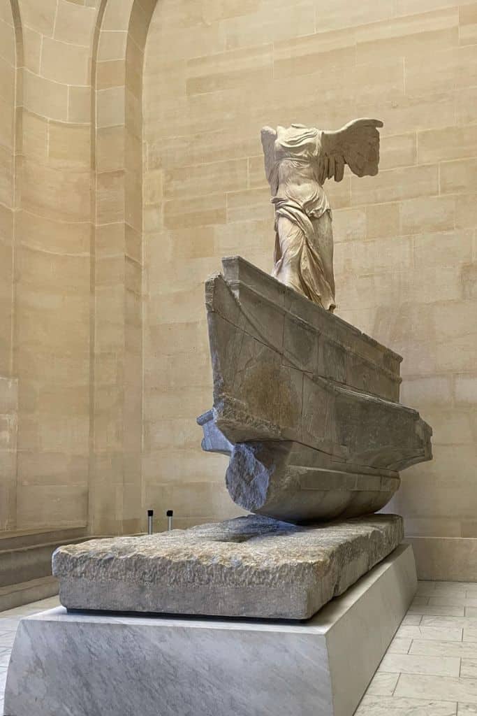 A sculpture of a headless winged woman standing on a jutting rock is found in the Louve art museum in Europe.