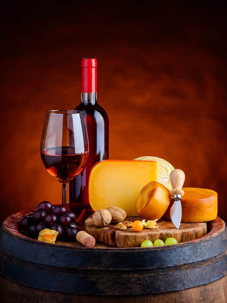 a wooden barrel has gouda cheese and a bottle of red wine on top of it with a red background