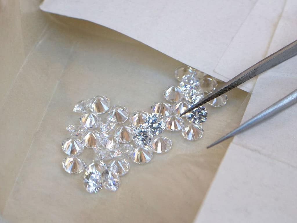 a pair of tweezers hover over a small grouping of diamonds on a brown sheet of paper