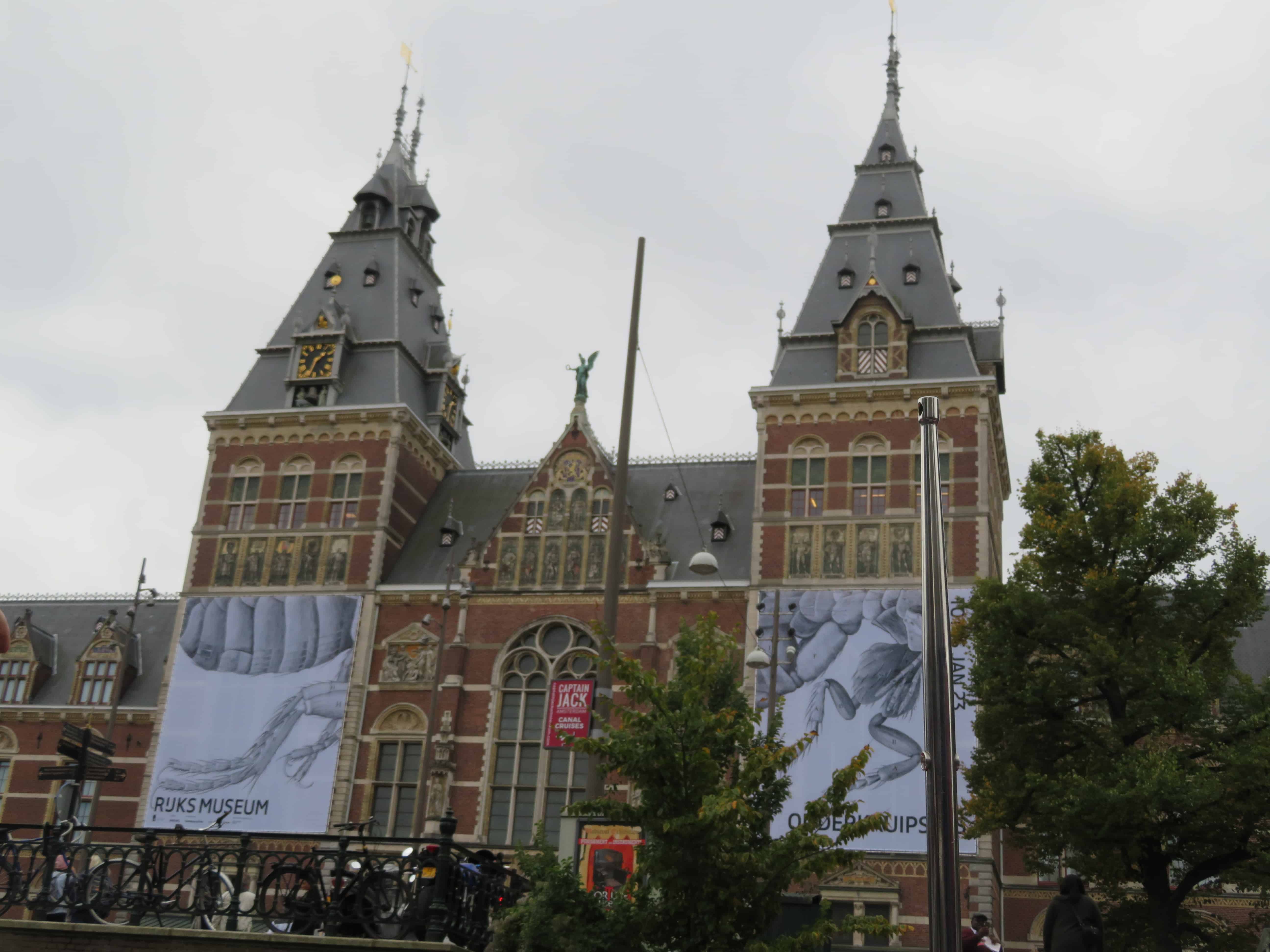 A brick building with tan trim and two large square columns make up the Rijksmuseum in Amsterdam.  The art museums are just one reason why Amsterdam is worth visiting.