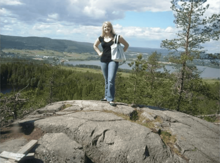 A young blonde-haired woman is standing on a large rock in Sweden.  Traveling the world changed her life and personality as it lead her to discover her love of language.