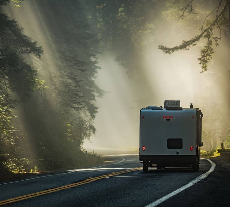 A RV camper drives down a curved road lined with trees.  Camping is a great way to experience an accessible road trip.