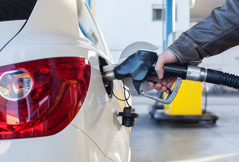 The hand of a white person is holding a black gas pump as they pump gas into a white vehicle.