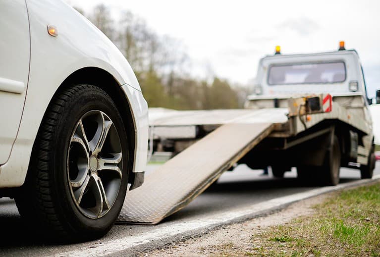 A white vehicle is behind the ramp of a tow truck.  Being prepared for anything on your accessible road trip is essential.