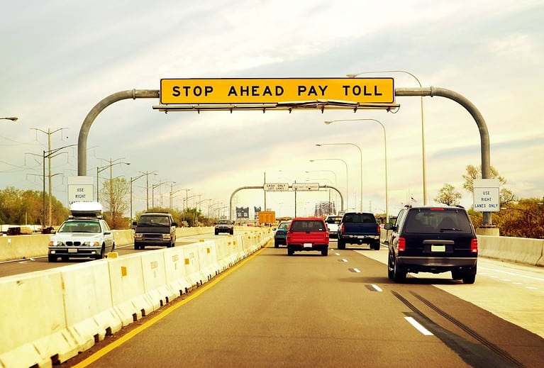 Several cars drive along a highway with a yellow sign overhead that says "stop ahead pay toll"