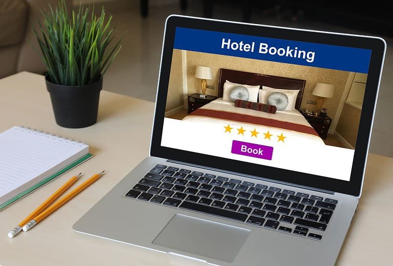 A laptop sits on a white desk and has a hotel booking screen on display