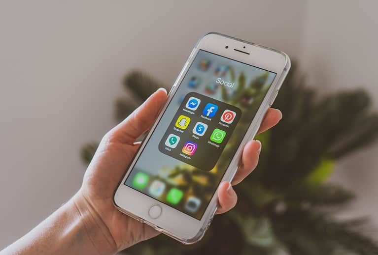 A white woman holds a cell phone displaying various apps