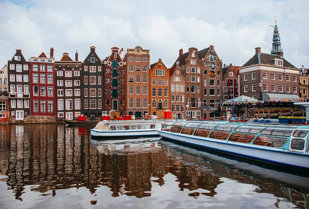 Two boats cruise along Amsterdam's famous canals in front of gingerbread style buildings.